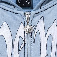 Load image into Gallery viewer, Close up of a treated and washed baby blue zip hoodie with white embroidered Revenge arch logo with black outline embroidery and a silver R zipper puller