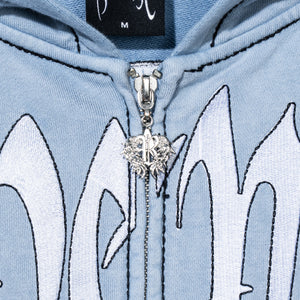 Close up of a treated and washed baby blue zip hoodie with white embroidered Revenge arch logo with black outline embroidery and a silver R zipper puller