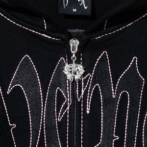 Close up of a black zip hoodie with black embroidered Revenge arch logo with pink contrast stitch outline embroidery and a silver R zipper puller