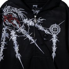 Load image into Gallery viewer, Close up of a black zip hoodie with white and red intricate designs on a dark background and distressed fabric
