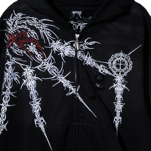 Close up of a black zip hoodie with white and red intricate designs on a dark background and distressed fabric